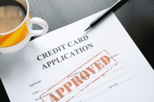 Credit card application form with an "APPROVED" stamp and a coffee cup on the table