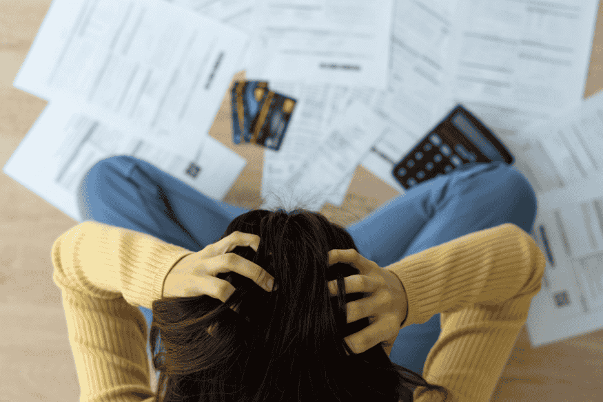 Overhead view of a stressed woman surrounded by bills, credit cards, and a calculator