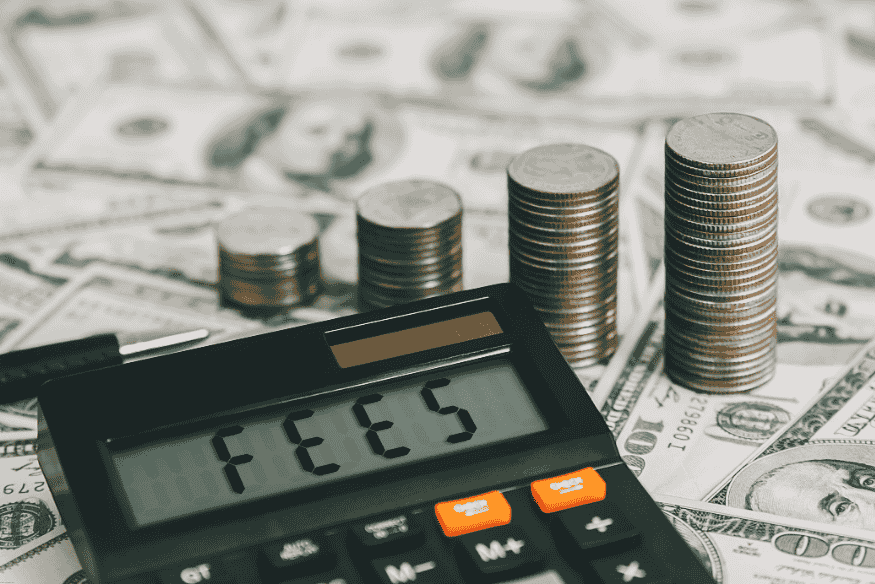 Calculator displaying the word “FEES” with stacked coins and dollar bills in the background