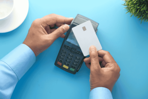 Person holding a white credit card near a payment terminal, ready to make a contactless transaction