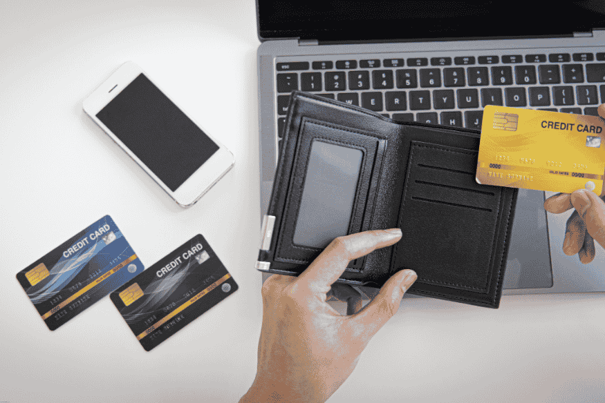 Person selecting a credit card from a wallet while shopping online on a laptop.